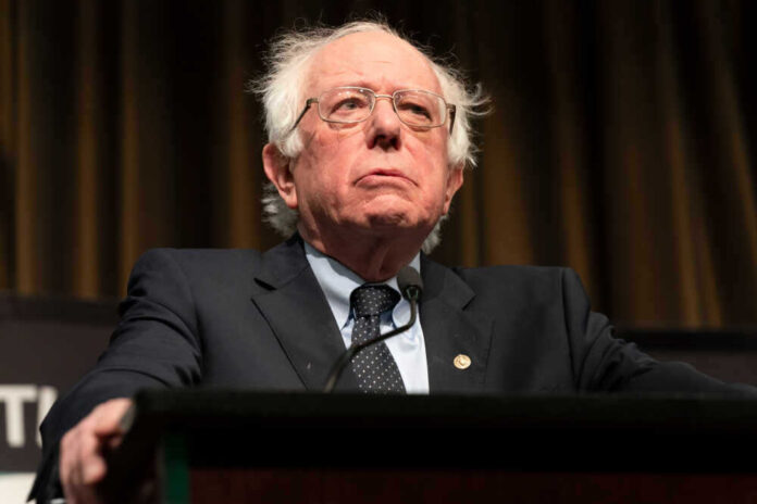 shutterstock_1360787486.jpg featured image Bernie Sanders in suit speaking at podium.