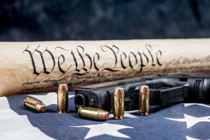 shutterstock_1864724608.jpg featured image Gun, bullets, Constitution scroll on American flag.
