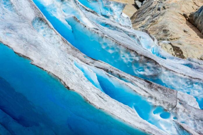 shutterstock_2496669217.jpg featured image Blue glacier ice with crevasses and rocky surface