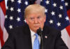 Donald Trump speaking with American flags in background.