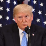 Donald Trump speaking with American flags in background.