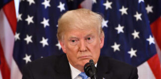 Donald Trump speaking with American flags in background.
