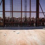 People standing behind a fence on a dusty path.