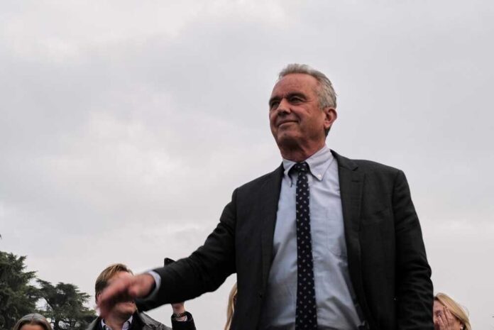 shutterstock_2314907207.jpg featured image Robert F. Kennedy Jr. in a suit stands outdoors, cloudy sky background.
