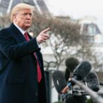 Man speaking to microphones, pointing outdoors.