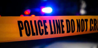 Police tape with flashing lights in the background