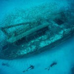 Underwater shipwreck with divers and school of fish.