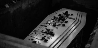 Coffin with flowers inside a dark burial plot