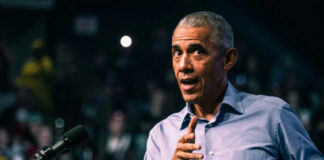 Barack Obama in blue shirt speaking at podium with microphone
