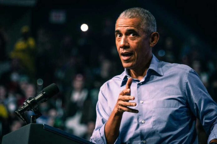 shutterstock_2231134745.jpg Barack Obama in blue shirt speaking at podium with microphone