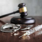 A gavel, handcuffs, and a syringe on a wooden surface