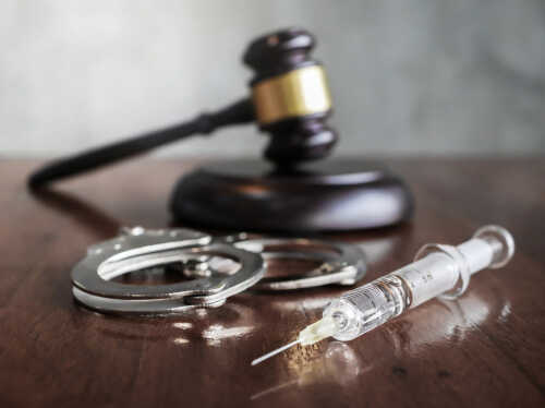 A gavel, handcuffs, and a syringe on a wooden surface