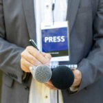 Legendary Reporter Witnessed Democracy’s Darkest Secrets Journalist with press badge, notebook, and microphones.