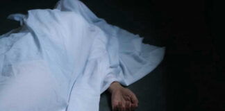 Hand emerging from under white sheet on dark surface