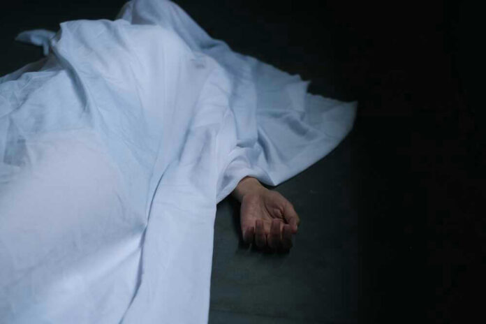 Hand emerging from under white sheet on dark surface