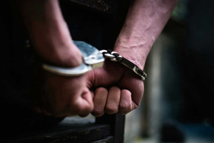 shutterstock_1338116366.jpg Close-up of hands in handcuffs behind back