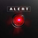 Red alert light against black background, text ALERT