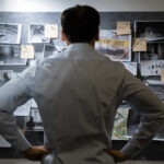 Operation Midway Blitz UNCOVERS 3,000 Criminals! Man examining investigation board with photos and notes.