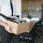 Person carrying box of office supplies in workspace.