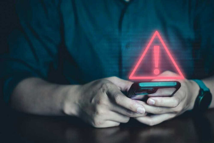 shutterstock_2342619545.jpg Person holding phone with warning symbol displayed