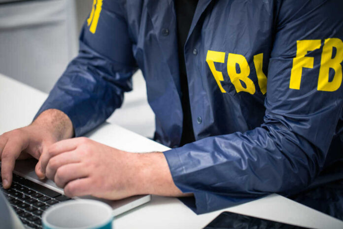 shutterstock_629482379.jpg Person in FBI jacket working on laptop.