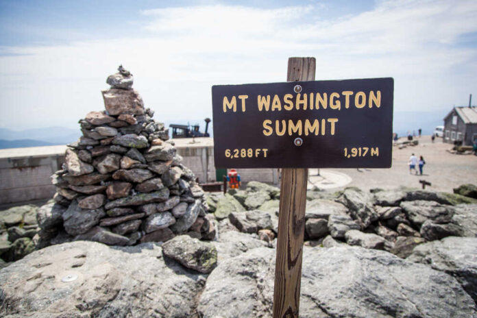 Sign indicating the summit of Mount Washington with a stone pile in the foreground