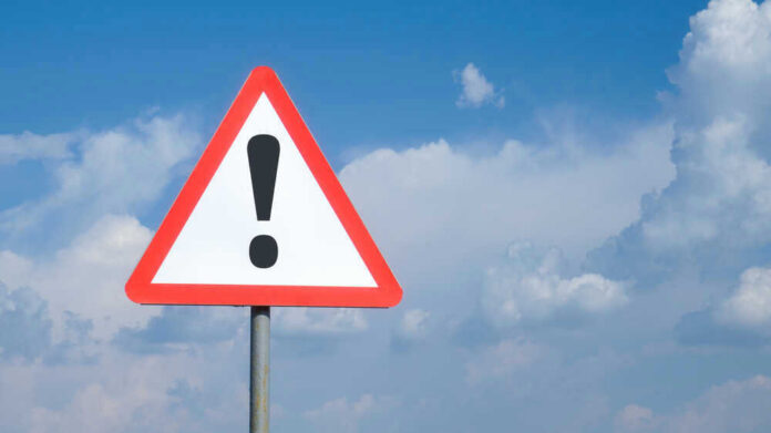 shutterstock_1783779719.jpg Triangle warning sign with exclamation mark against sky.
