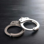 Three Boys VANISHED — Dad Finally Faces Justice Metal handcuffs on a dark textured surface.