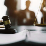 Federal Judge PUNISHES Officials for Following Law Gavel and scales in courtroom with blurred figures behind.