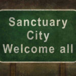 Trump’s Army Targets Sanctuary Cities NEXT Green sign reading Sanctuary City Welcome all