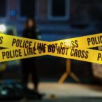BLOODBATH Triggers Another Immigration Crackdown Police tape marking a crime scene with blurred figures in the background