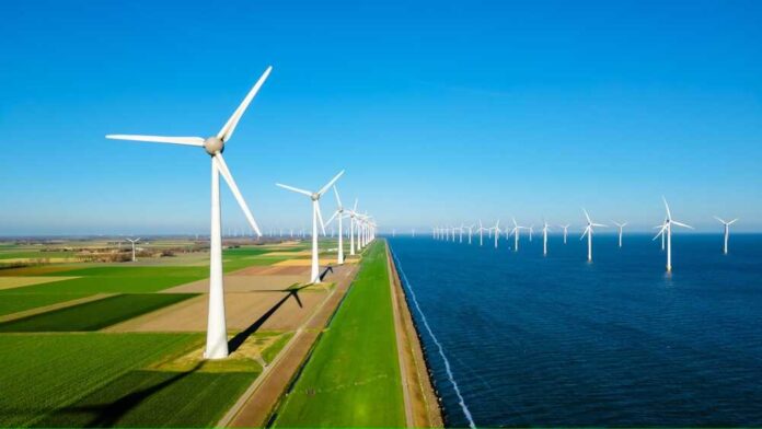 A row of wind turbines along a coastal area with fields and blue sky