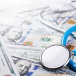 A stethoscope resting on a pile of hundred-dollar bills