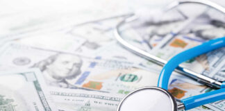 A stethoscope resting on a pile of hundred-dollar bills