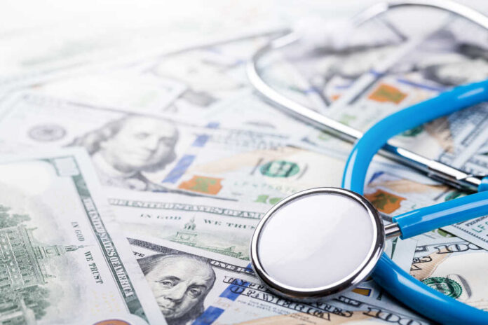 A stethoscope resting on a pile of hundred-dollar bills