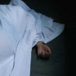 Hand emerging from under white sheet on dark surface.