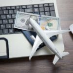 A model airplane on a laptop keyboard with a passport and cash