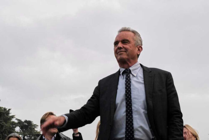 Robert F. Kennedy Jr. in a suit stands outdoors, cloudy sky background.