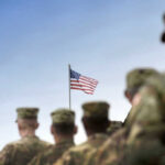 Trump Threatens to Unleash 1,500 Troops Soldiers in uniform with American flag in background.