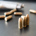 Mass Shooter’s Chilling Plot Exposes Security Flaws Close-up of bullets on a dark surface with a handgun in the background