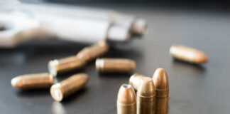 Close-up of bullets on a dark surface with a handgun in the background
