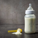 A baby bottle filled with milk next to a scoop of powdered formula