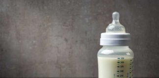 A baby bottle filled with milk next to a scoop of powdered formula