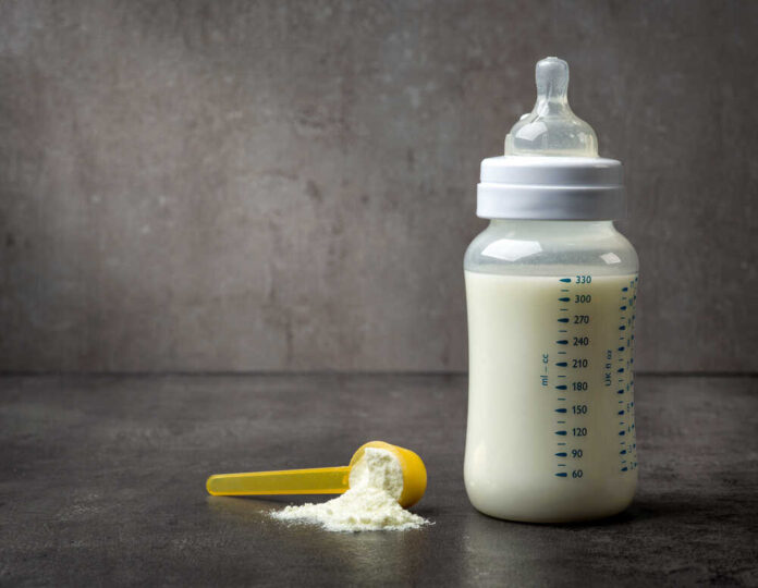 A baby bottle filled with milk next to a scoop of powdered formula