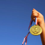 Olympic Medals FALL Apart On Camera A hand holding a gold medal against a clear blue sky