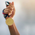 A hand holding a gold medal with a ribbon