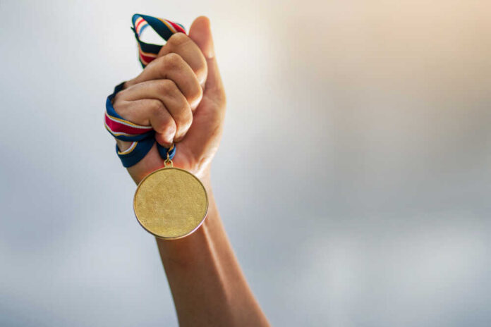 A hand holding a gold medal with a ribbon