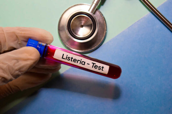 A gloved hand holding a blood test tube labeled 'Listeria - Test'