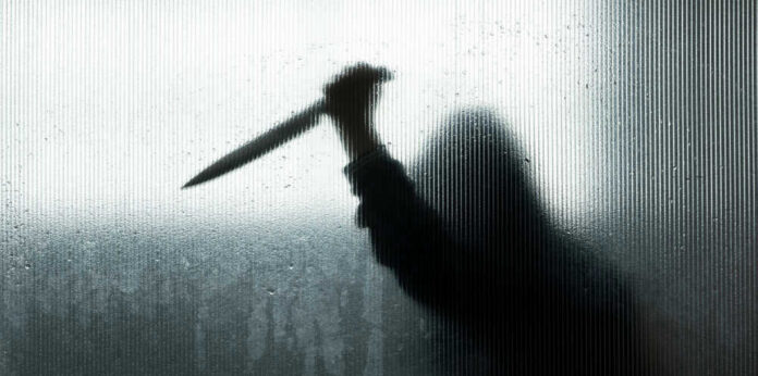 Backlit silhouette holding a knife through frosted glass.