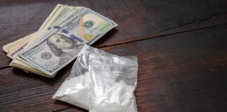 Bundles of cash next to bags of white powder on a wooden surface